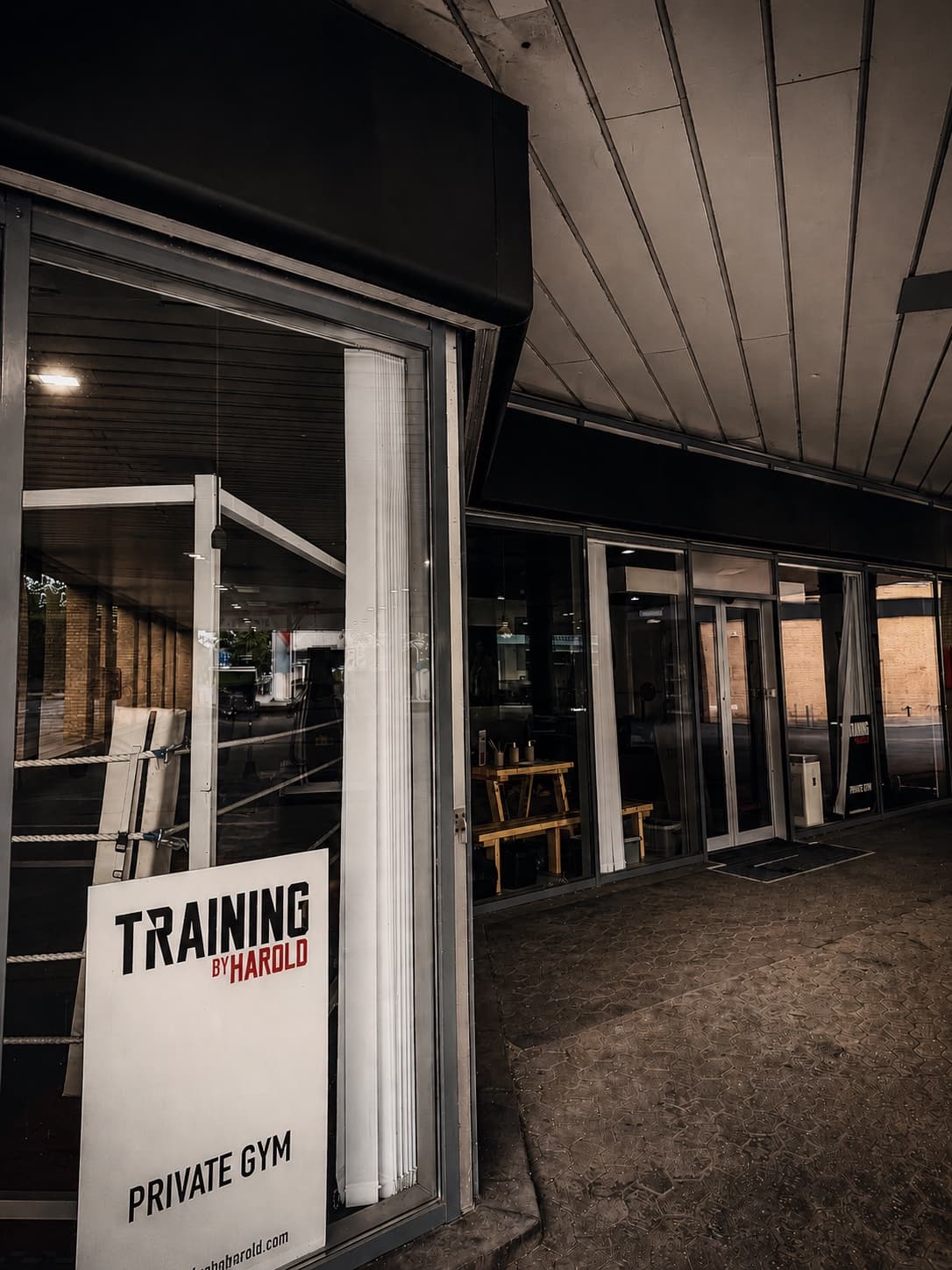 The entrance of Training by Harold's private gym at Strandvejen 70 in Hellerup — the sign in the glass facade, with the boxing ring visible inside